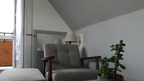 Une pièce comprenant un fauteuil à revêtement gris, une table en bois, une plante en pot et une lampe fixée au mur.