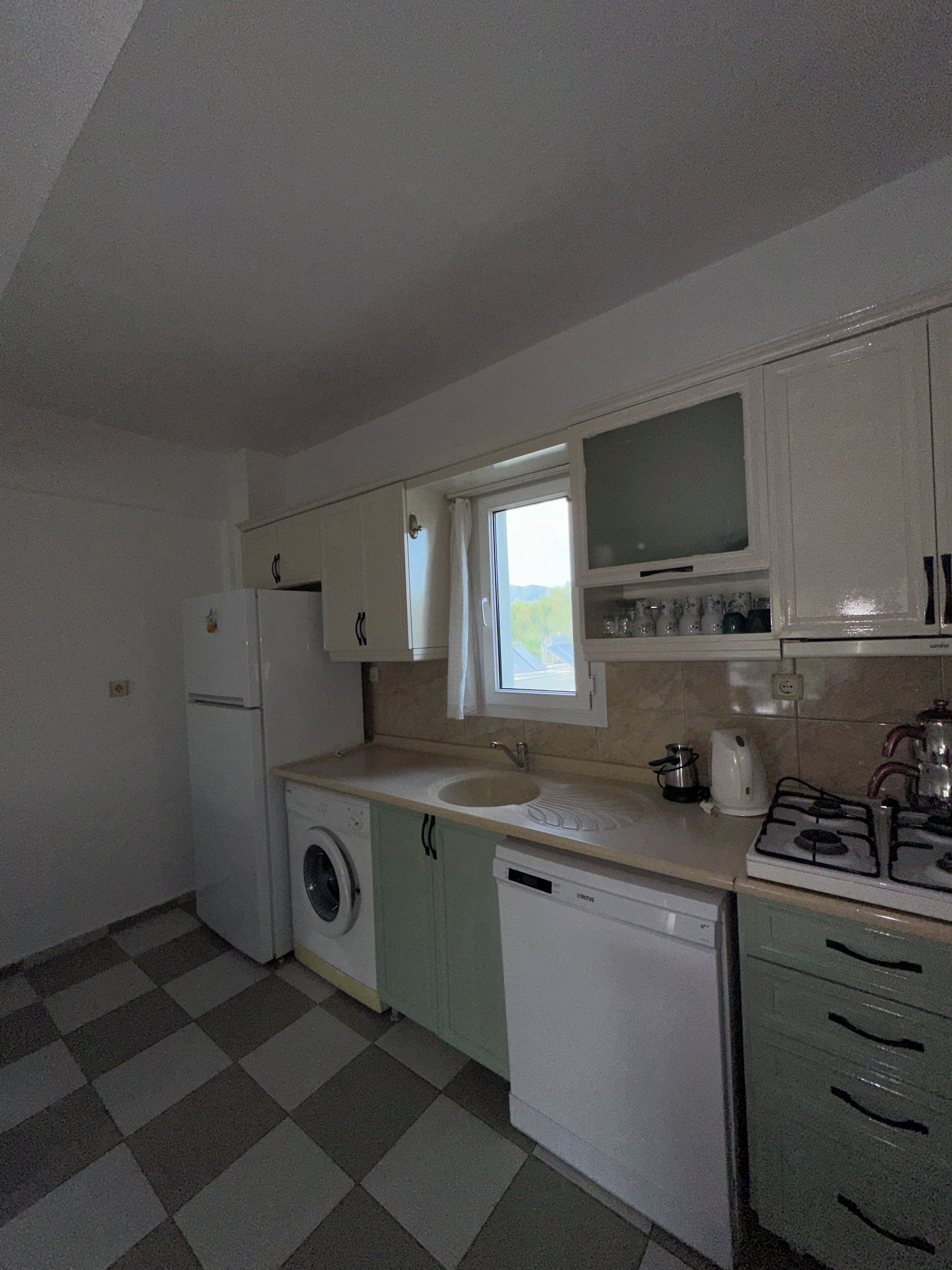 A compact kitchen with basic appliances, a washing machine, and a window providing natural light.