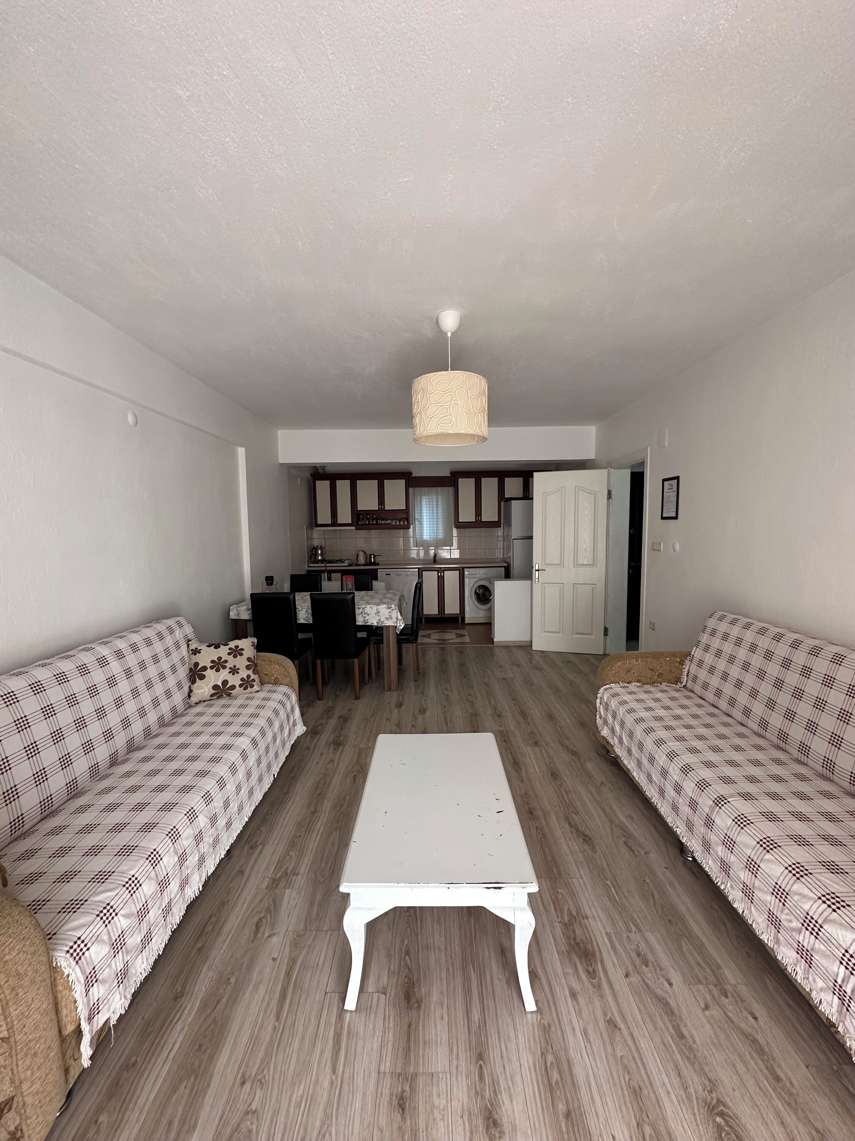 Una sala de estar con dos sofás, una mesa de centro y una cocina al fondo.