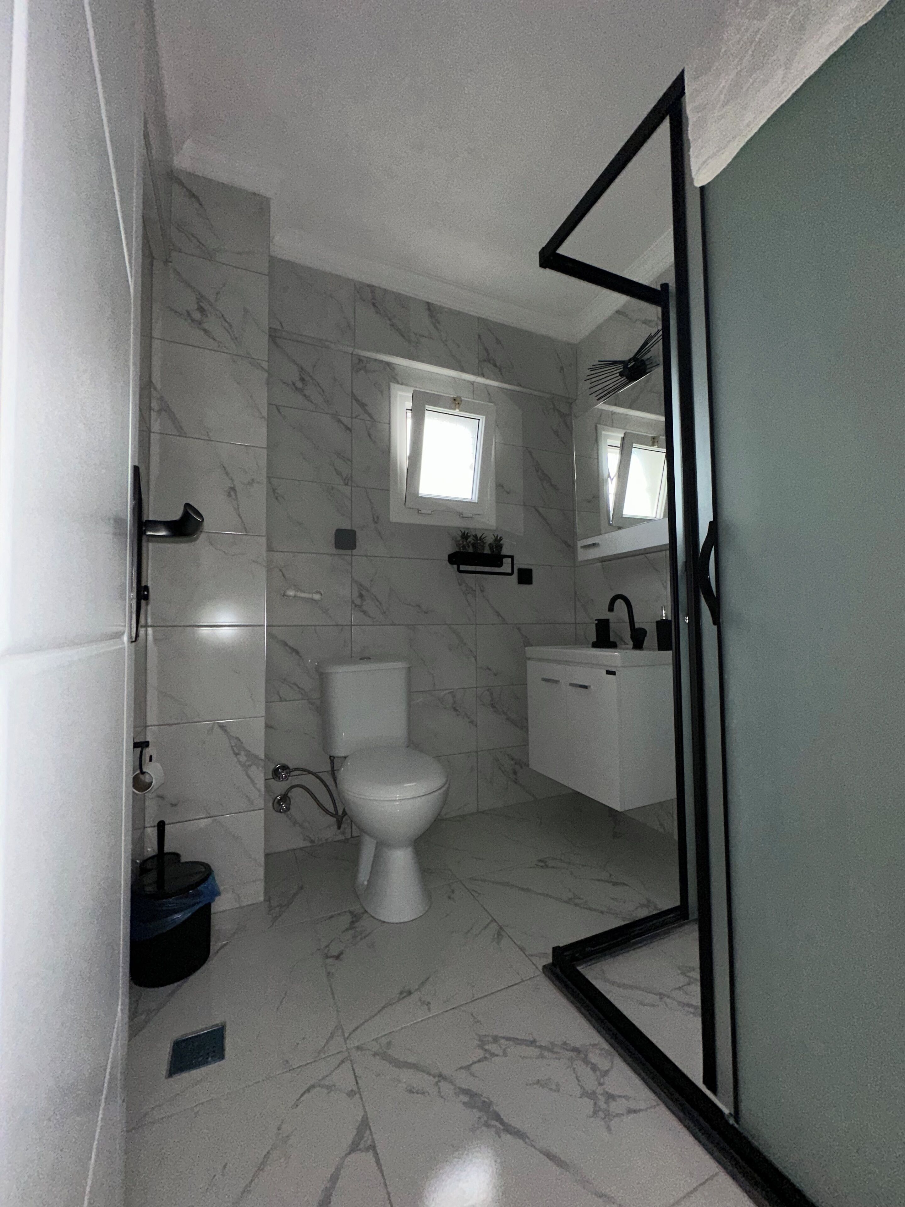 A bathroom with a toilet, a sink, a shower area, and a small window.