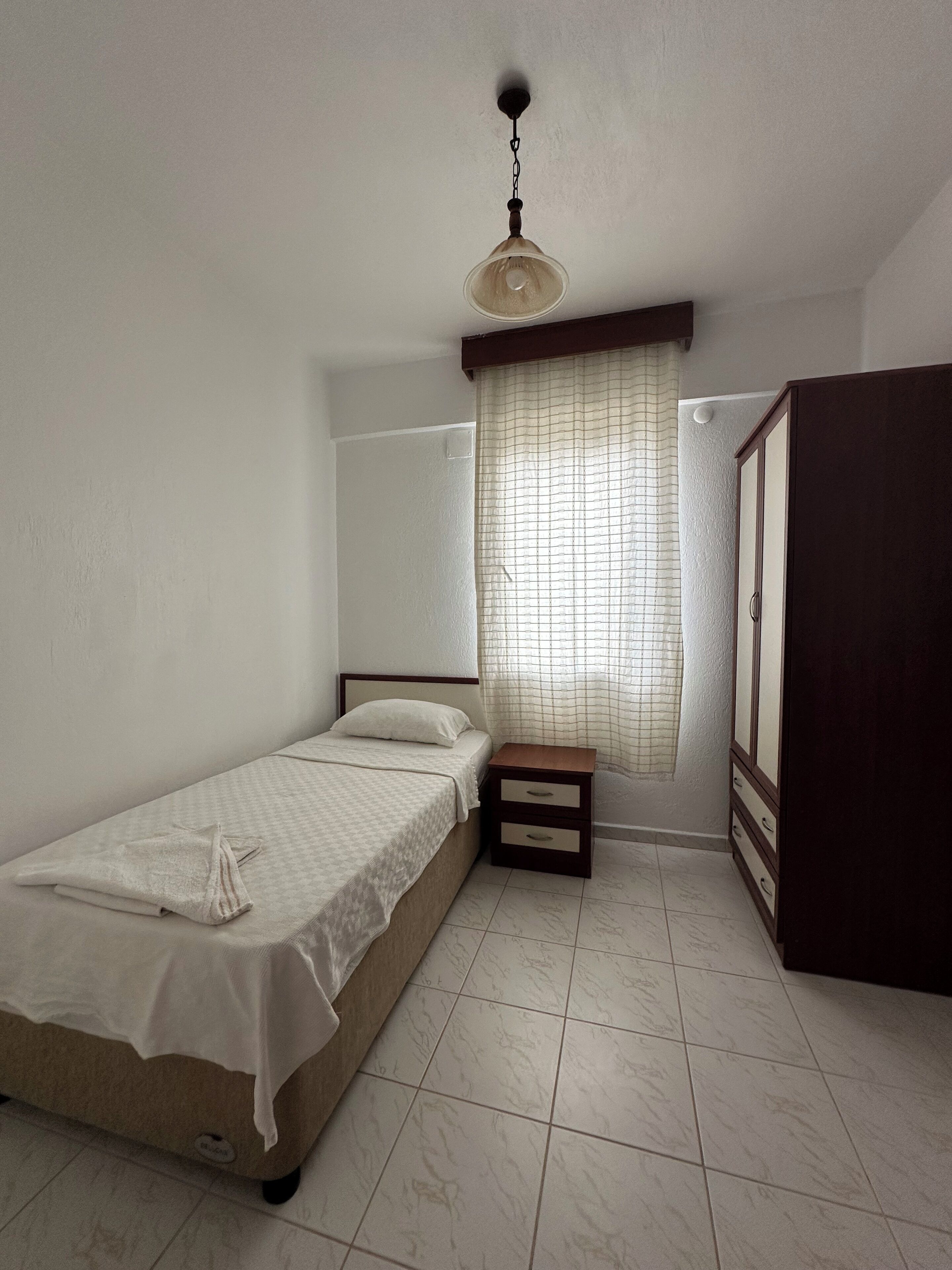 Een slaapkamer met een enkel bed, een nachtkastje, een garderobe en een plafondlamp.