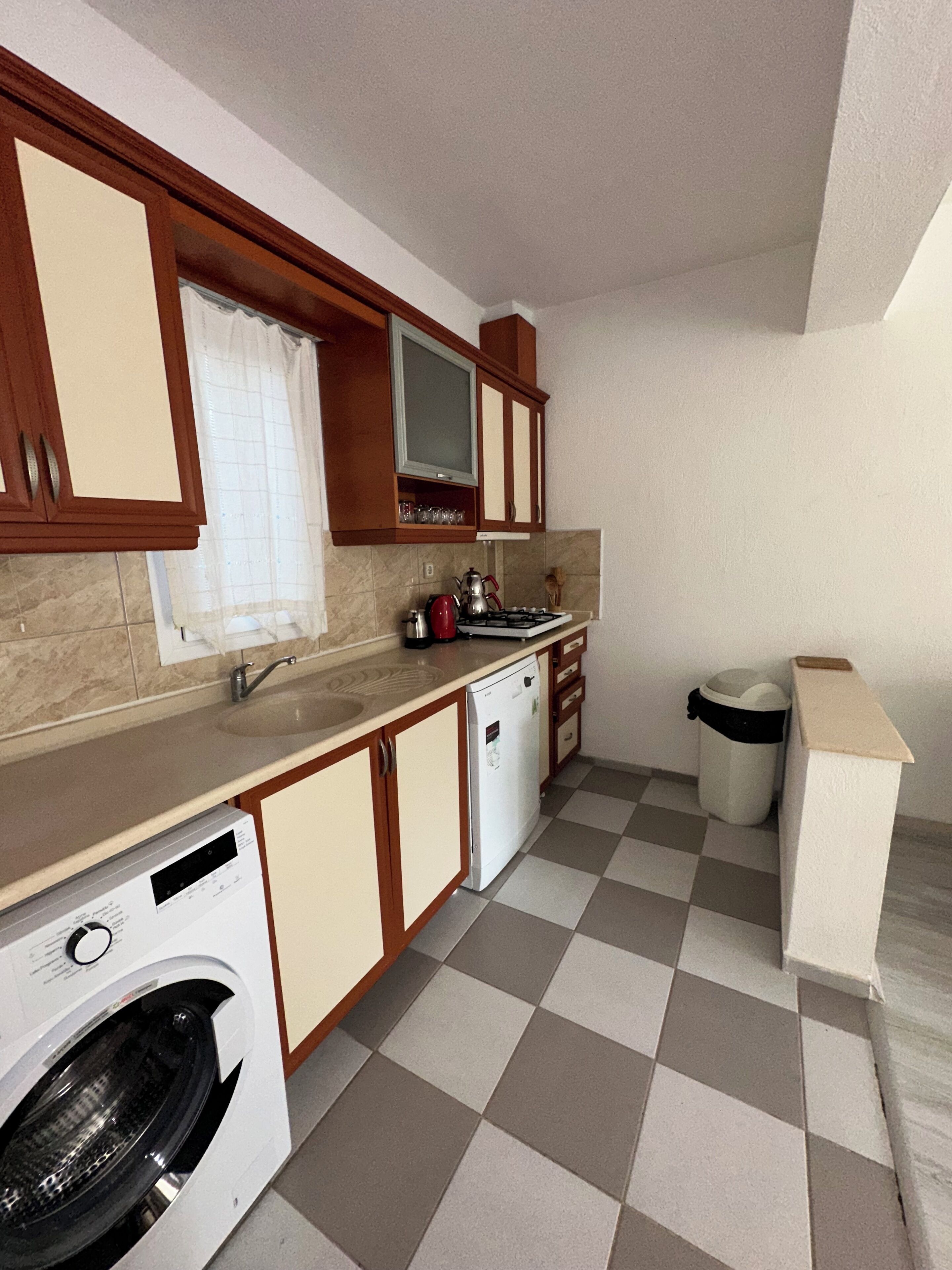 Una cucina compatta con lavatrice, lavello e cestino.