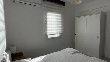 Un dormitorio con cama, ventana con persianas, equipo de aire acondicionado, armario y lámpara colgante.