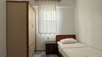 Um quarto com uma cama, guarda-roupa, mesa de cabeceira, janela com cortinas e luminária no teto.