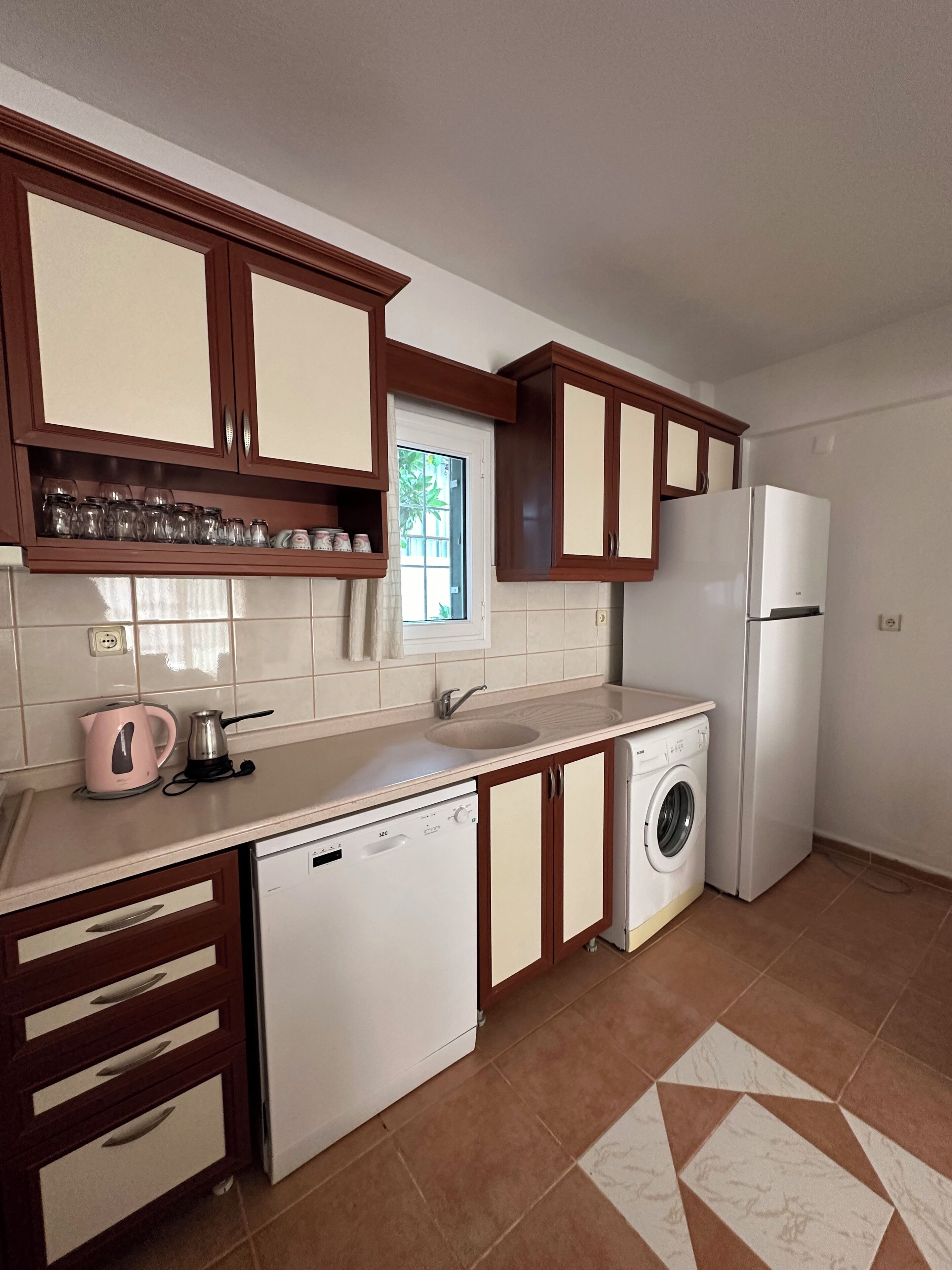 Eine Küche mit Holzausstattung, einem weißen Kühlschrank, einer Waschmaschine und einer Kaffeemaschine.