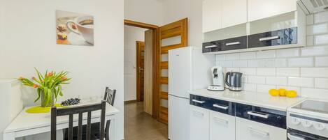A modern kitchen with white cabinets, a coffee machine, and a dining area with a table and chairs.