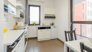 A compact kitchen with white cabinets, a built-in microwave, and a window with a view of buildings. - ShortStayPoland Skierniewicka B156 (Warsaw)