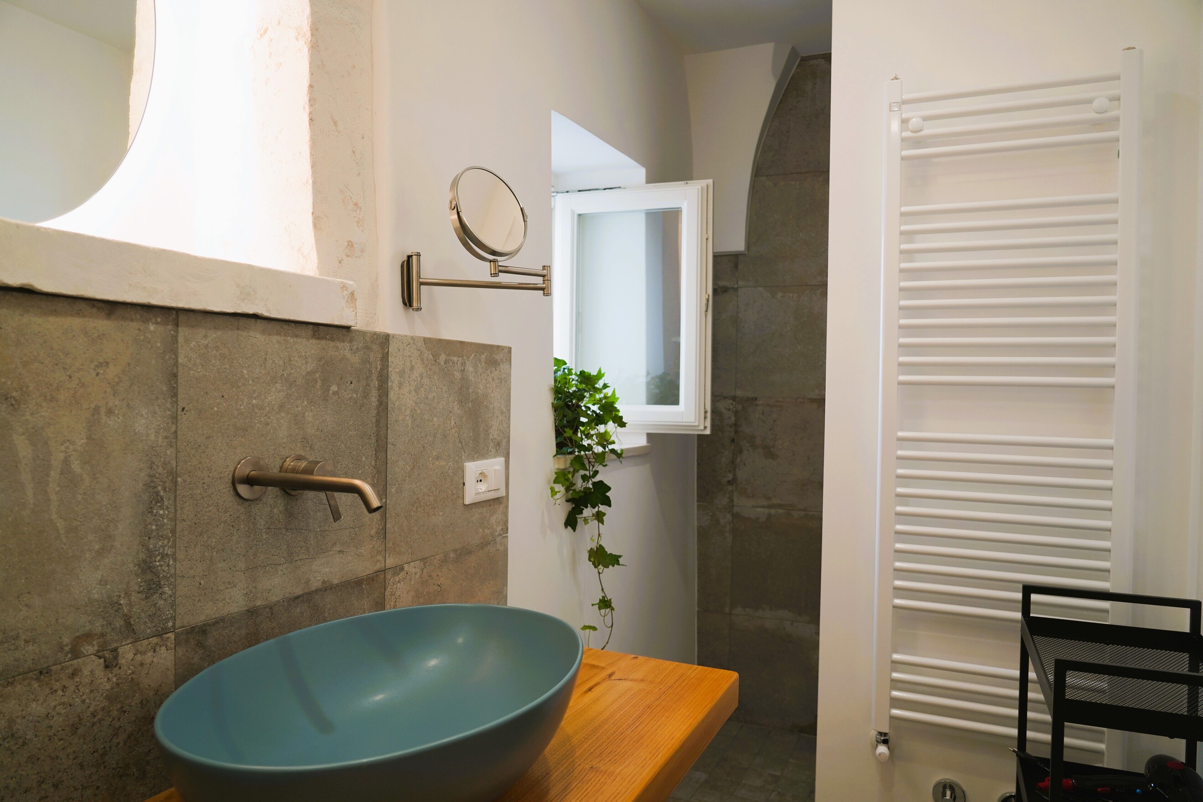 A bathroom with a large blue basin, a wooden countertop, a towel rack, a mirror, and a white towel dryer.