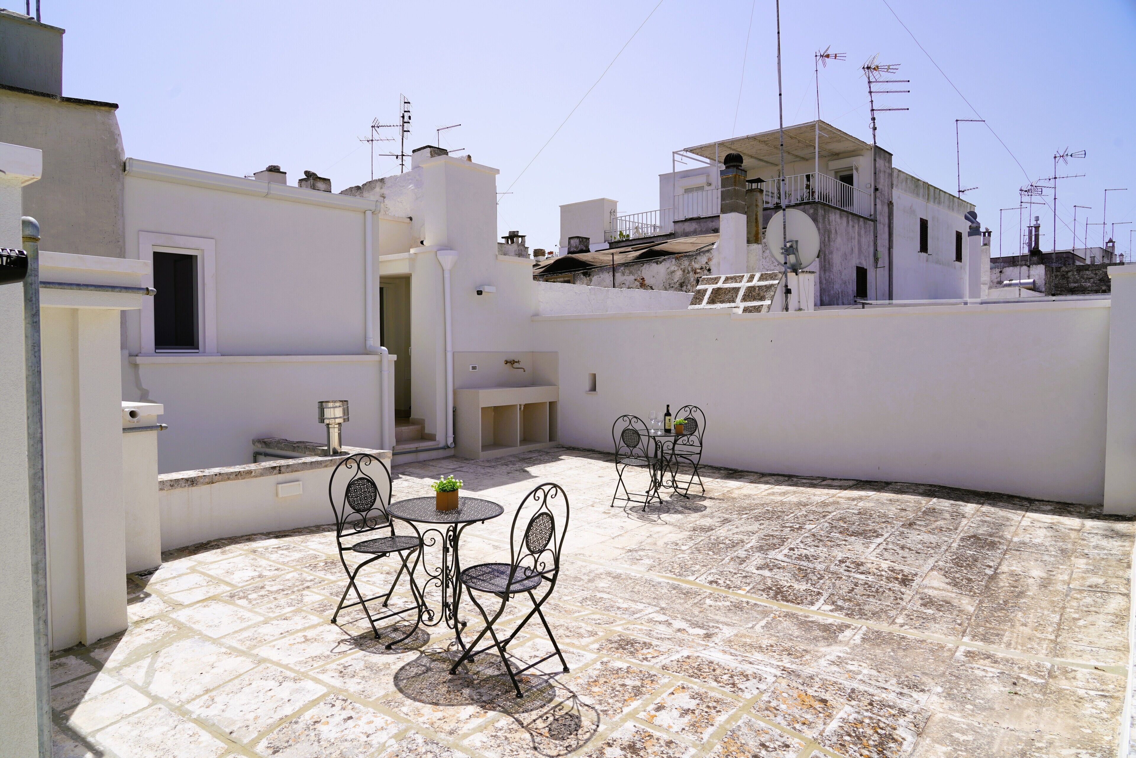 A rooftop patio with outdoor seating, a small table with a plant, and a view of surrounding buildings.
