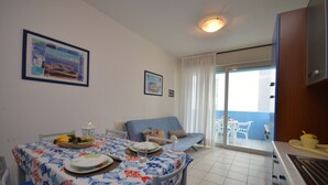 Un coin repas avec une table dressée pour deux personnes, un canapé et une vue sur le balcon.