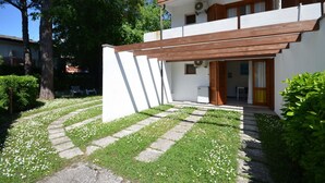 Une maison moderne à deux étages, avec une façade blanche, un balcon en bois et un chemin en pierre menant à l’entrée.