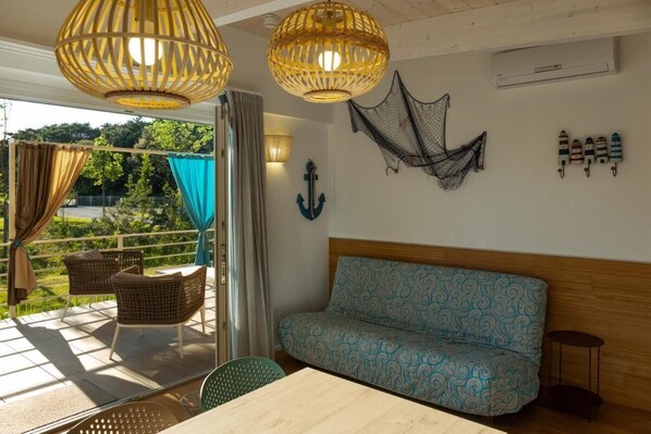 A room with a wooden sofa, wicker chairs, a table, and a view of greenery outside.