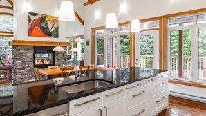 A modern kitchen with a large island, stone fireplace, and large windows offering views of the outdoors.