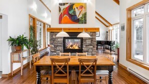 A spacious dining area with a stone fireplace, wooden ceiling beams, and large windows.
