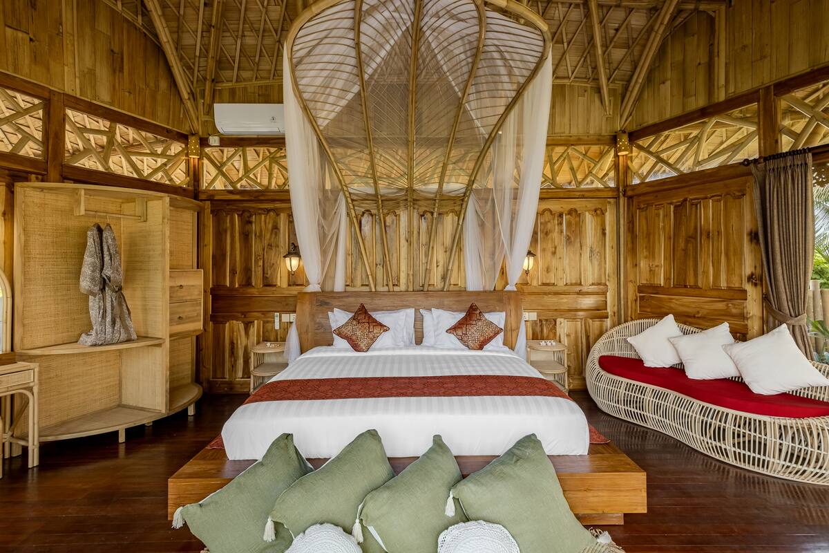 A wooden room with a bed, a wicker sofa, and a statue.