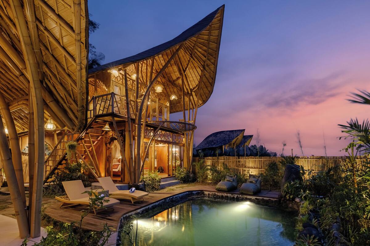 A modern resort with a pool, lounge chairs, and a bamboo structure.