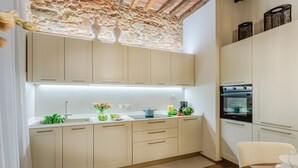 A modern kitchen with white cabinets, a built-in oven, and a stone accent wall. - Casa Cinnamon in Lucca (Lucca)