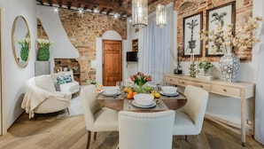 A dining area with a brick wall, wooden ceiling, and a wooden dining table set for four. - Casa Cinnamon in Lucca (Lucca)