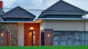 A two-story house with a stone facade, a wooden door, and a well-lit entrance. - Belvilla Wanderlust Central UbudNearTiti Batu Ubud Club (Ubud)