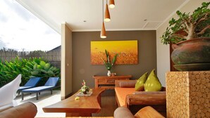 A modern living room with a wooden coffee table, cushioned seating, a large painting, and a potted plant. - Belvilla Wanderlust Central UbudNearTiti Batu Ubud Club (Ubud)