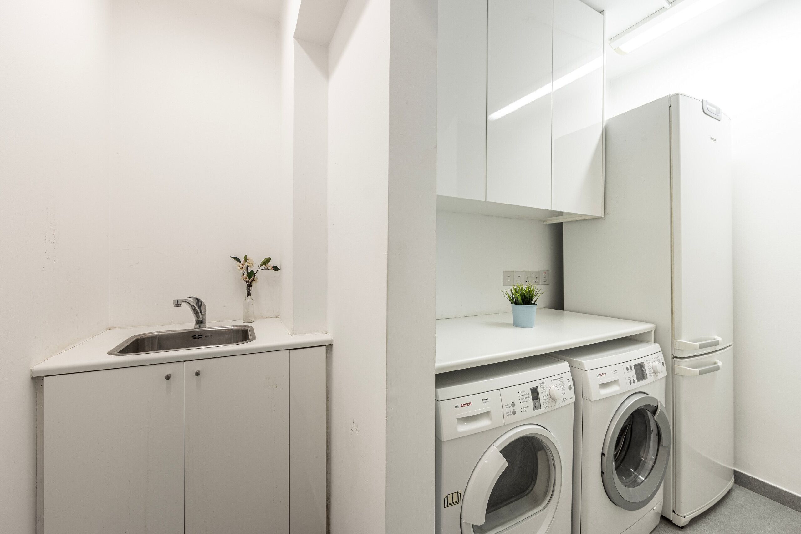 A modern laundry room with two Bosch washing machines, a sink, and a small potted plant.