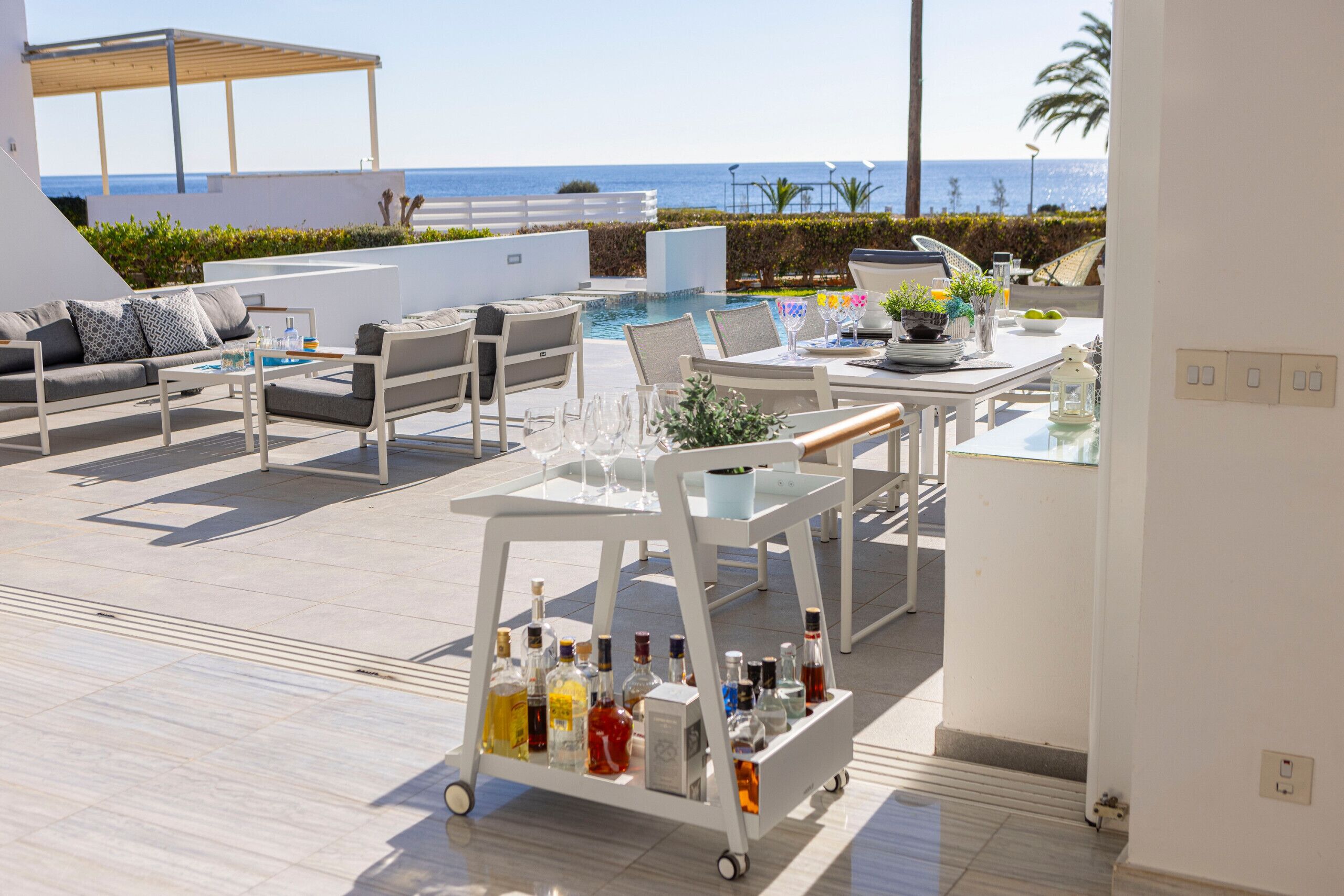 A modern outdoor lounge area with a pool, seating, and a cart with bottles.