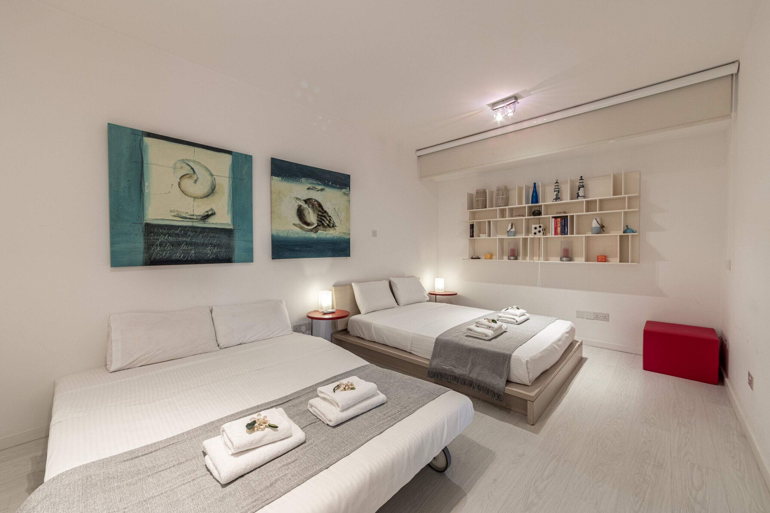 A hotel room with two beds, a bookshelf, and artwork on the walls.