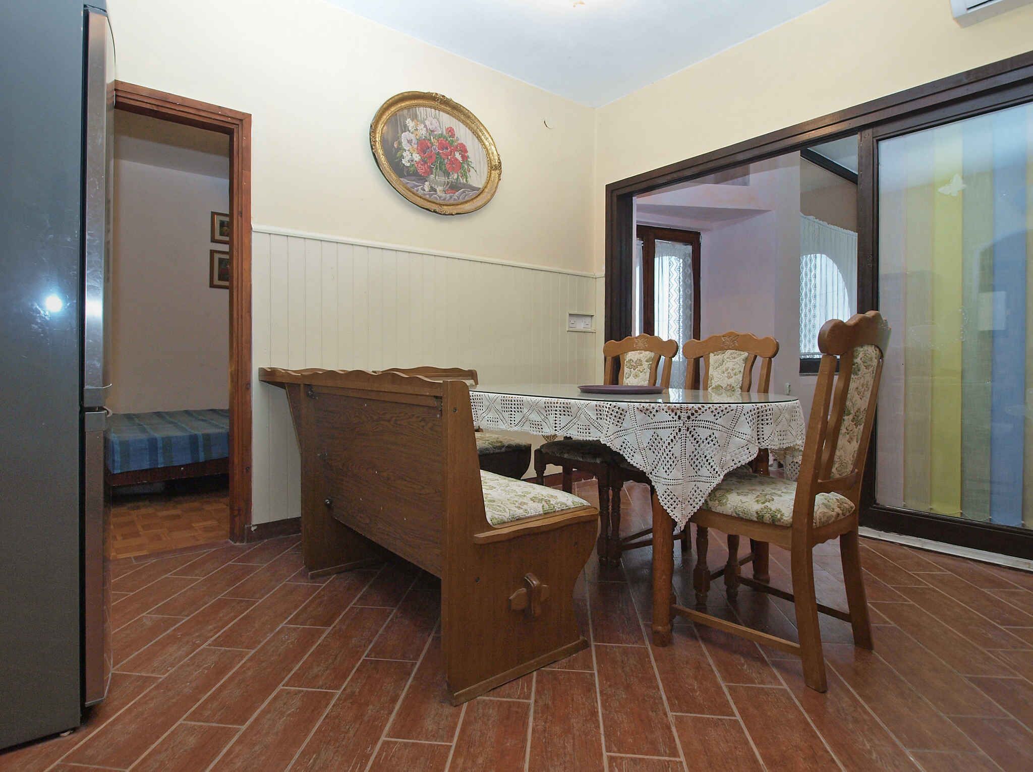 Ein Essbereich mit Holztisch und Stühlen, einer kleinen Bank, einem Kühlschrank und einem an der Wand hängenden Bild.