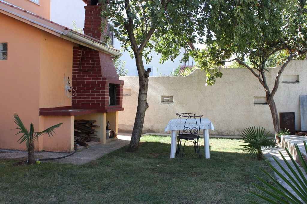A small patio area with a table and chairs, surrounded by a low brick wall and a tree.