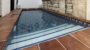 Una piscina con intrincados diseños de mosaicos, una pared blanca con placas decorativas y una pared de piedra con elaboradas esculturas.