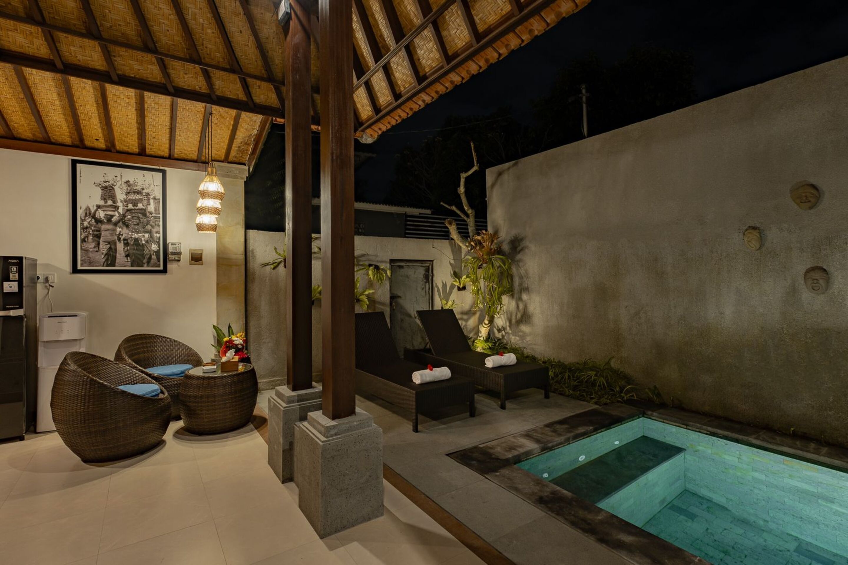 A poolside area with lounge chairs, a small pool, and a thatched roof structure.