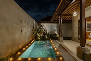 Una piscina con borde de azulejos, rodeada de velas y plantas, con una zona cubierta y estructura de techo de madera.