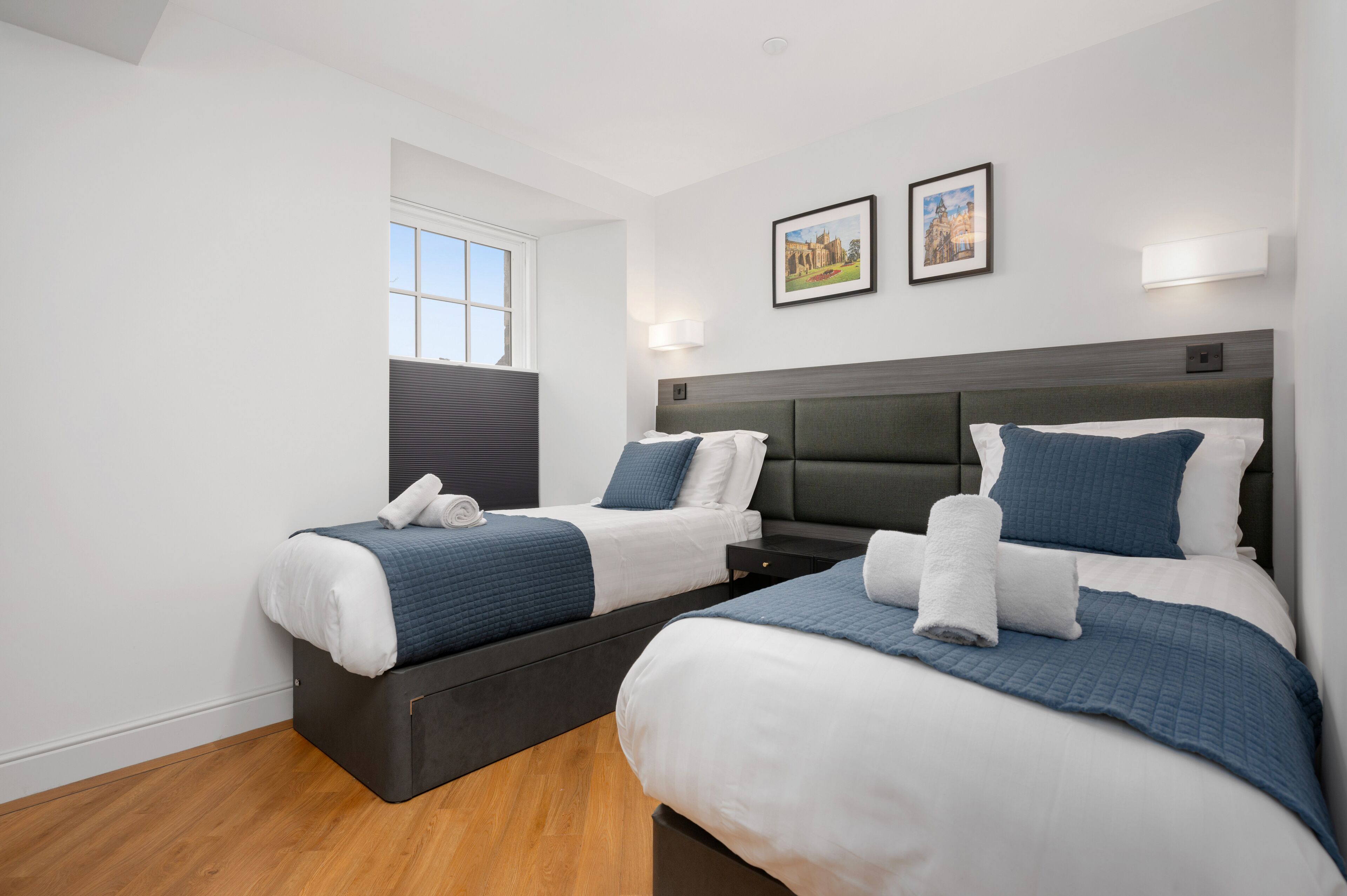 A hotel room with two beds, a window, and two wall-mounted lights.