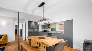 A modern kitchen with grey cabinets, a wooden dining table with benches, and a hanging light fixture. - 314 Reid's Corner - by Stay Dunfermline (Dunfermline)