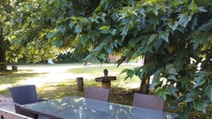 Ein Essbereich im Freien mit Tisch und Stühlen, umgeben von Bäumen und einem Garten.