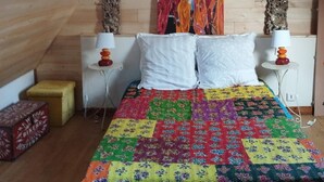Ein Schlafzimmer mit Holzbalkendecke, einem Bett mit bunter Steppdecke, zwei Nachttischen mit Lampen und einem Bild an der Wand.