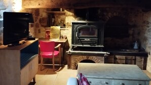 Ein rustikales Zimmer mit Steinwand, Fernseher, rotem Sessel, Holztisch und einer Couch.