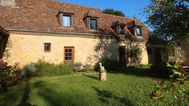 Ein Steinhaus mit geneigtem Dach, ein kleiner Garten mit einer Statue und einem strahlend blauen Himmel.