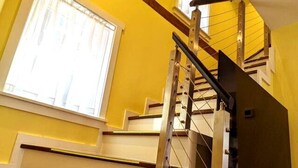 A staircase with a metal handrail and wooden steps, leading to a landing with a window. - Walkable Elmwood Cottage, No Chores 2Bath 2BR 2Car (Buffalo)