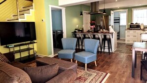 A living room with a TV, a staircase, and a dining area with bar stools. - Walkable Elmwood Cottage, No Chores 2Bath 2BR 2Car (Buffalo)