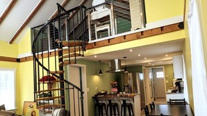 Un vaste espace de vie comprenant un escalier en bois, une table à manger et un coin cuisine avec un bar.