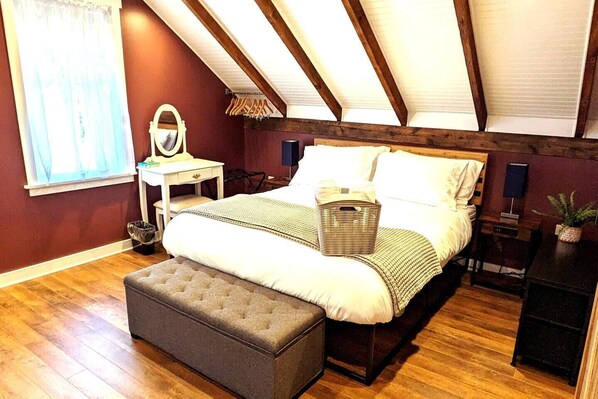 Un dormitorio con una cama grande, una mesita de noche, un aparador, un espejo y una ventana con cortinas.