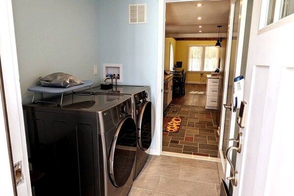 A laundry area with a washing machine and dryer, a bench, and a small table with a bag.