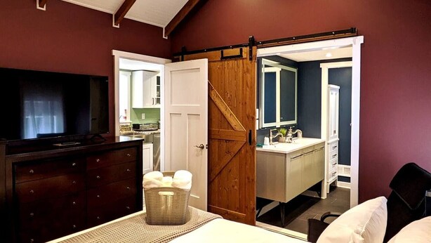 A bedroom with a bed, a dresser, a television, and a sliding door leading to a bathroom. - Walkable Elmwood Cottage, No Chores 2Bath 2BR 1Car (Buffalo)