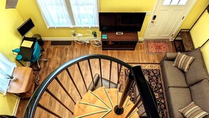 A modern living room with a wooden spiral staircase, a sofa, a TV, and a dining area with a table and chairs. - Walkable Elmwood Cottage, No Chores 2Bath 2BR 1Car (Buffalo)