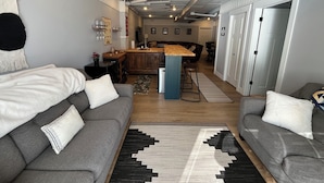 Una sala de estar moderna con sofás grises, una mesa de centro de madera y una alfombra blanco y negro.