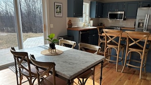 Una cocina moderna con armarios azules, encimera de mármol y una zona de comedor con sillas y mesa de madera.