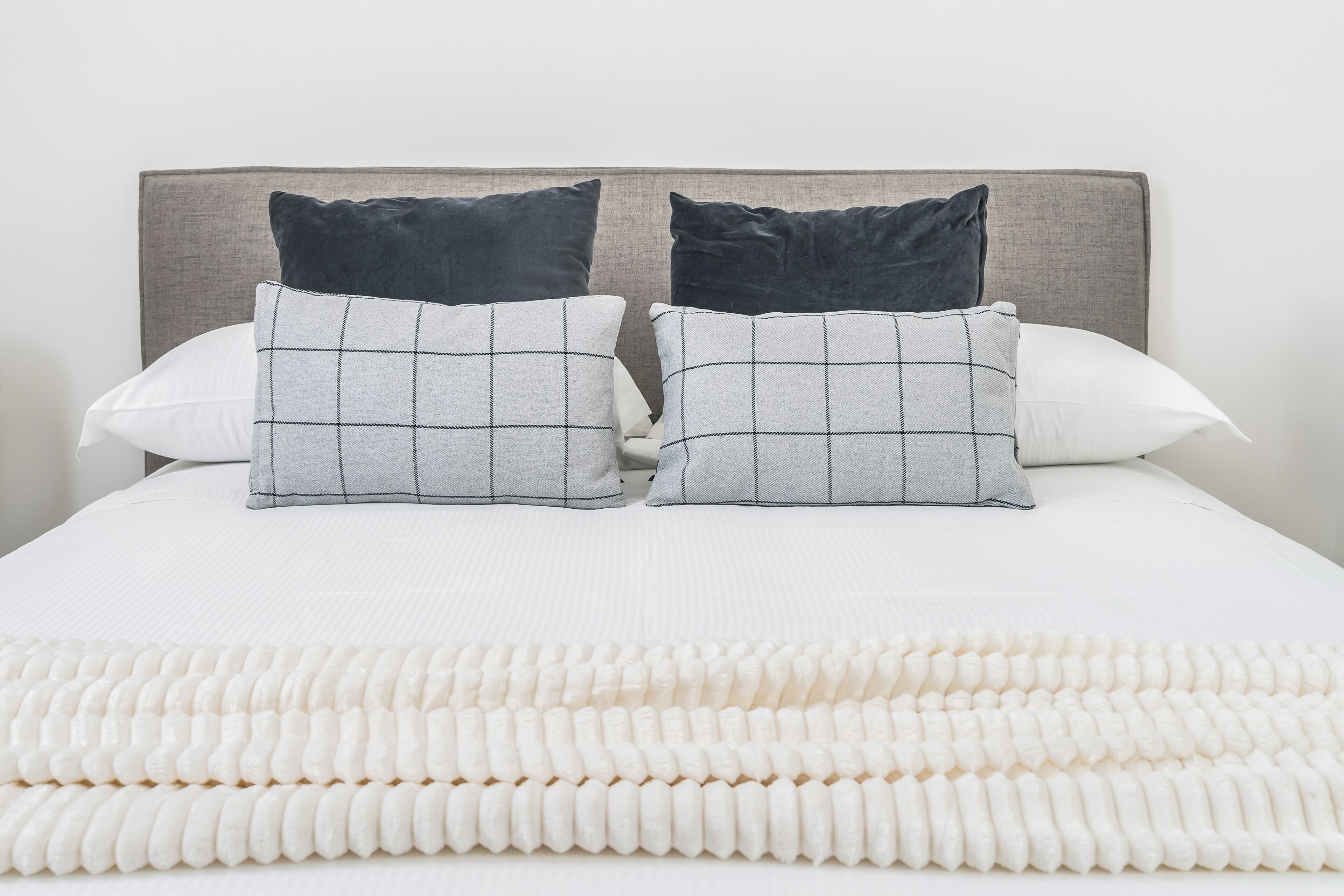 A neatly made bed with a white comforter and two pillows, one with a checkered pattern and the other plain.