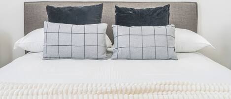 A neatly made bed with a white comforter and two pillows, one with a checkered pattern and the other plain.