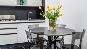 Una cocina moderna con encimera negra, armarios blancos, un lavamanos de acero inoxidable y un jarrón con tulipanes amarillos sobre una mesa redonda.